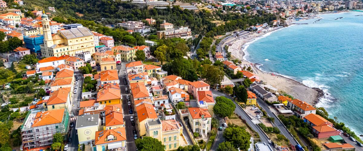 A coastal town with colorful buildings, a beach, and mountains in the background.