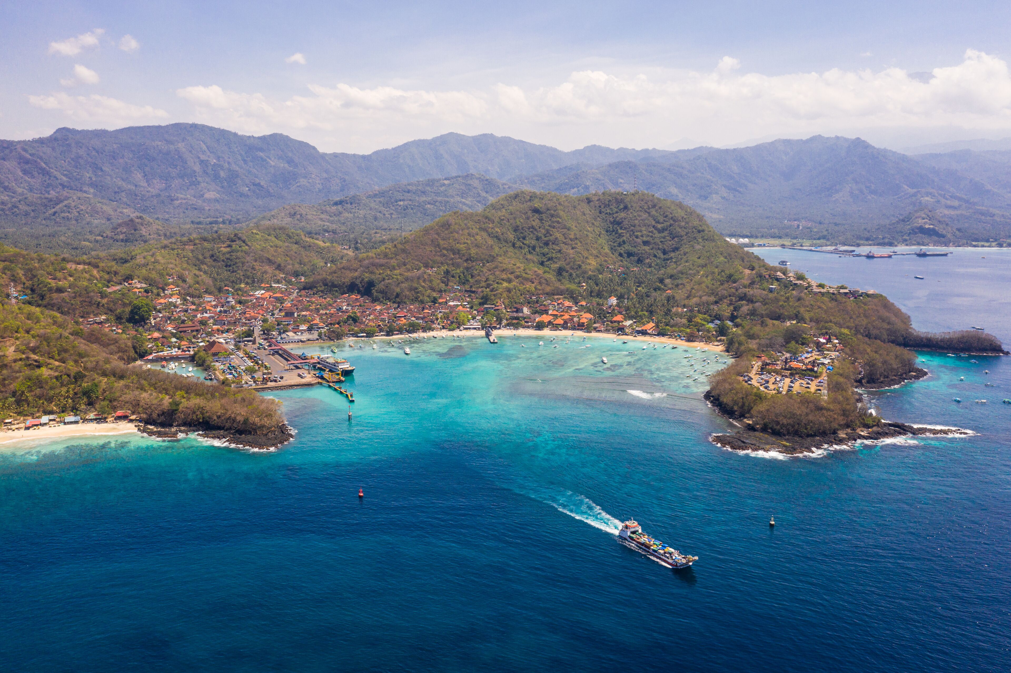 A coastal town with a marina, surrounded by mountains and clear blue waters.
