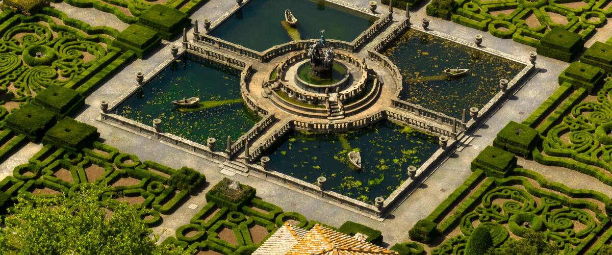 An aerial view of a formal garden with geometric hedges, a central fountain, and a symmetrical layout.