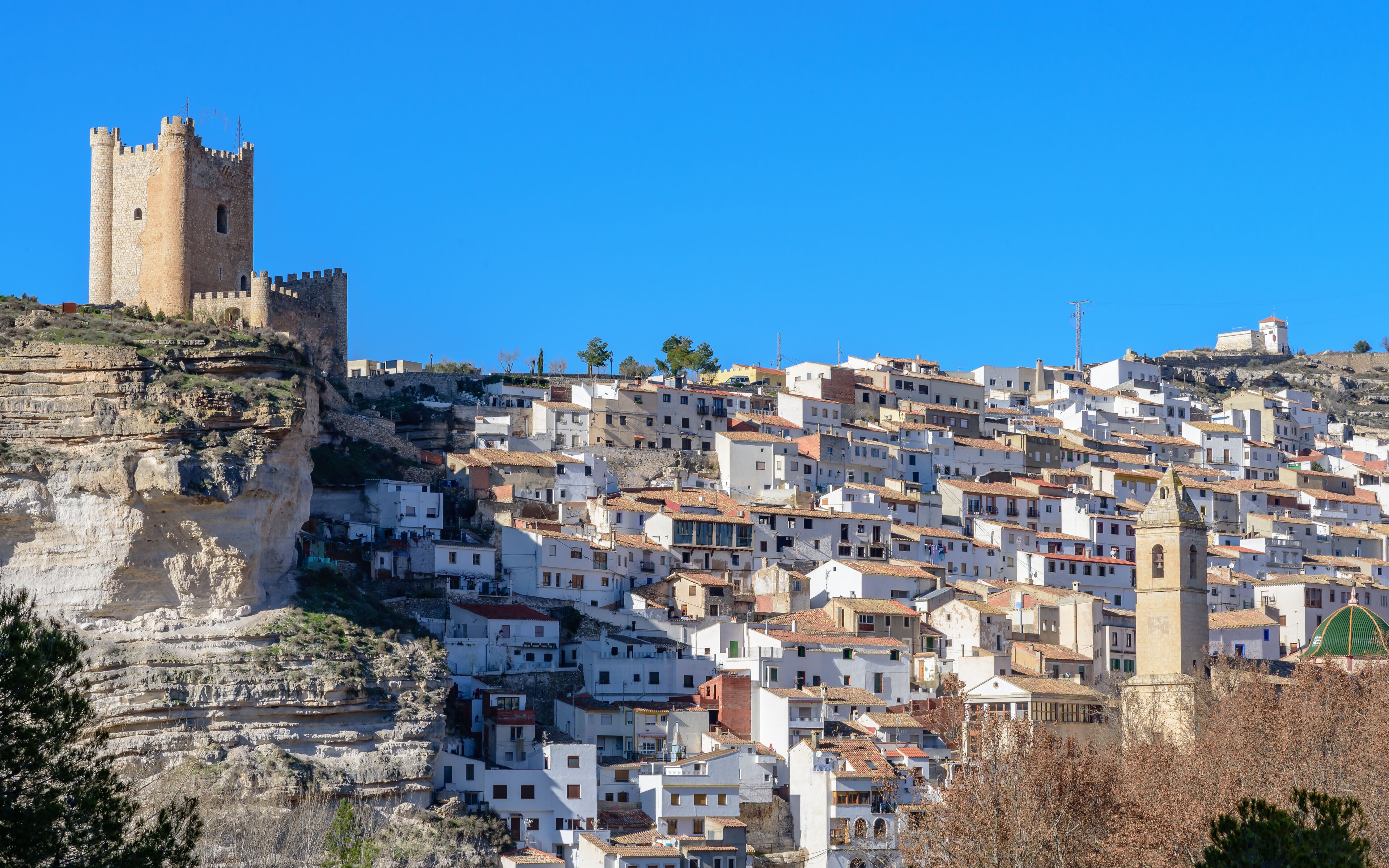 A historic town with a prominent castle on a cliff, terraced buildings, and a church with a green dome.