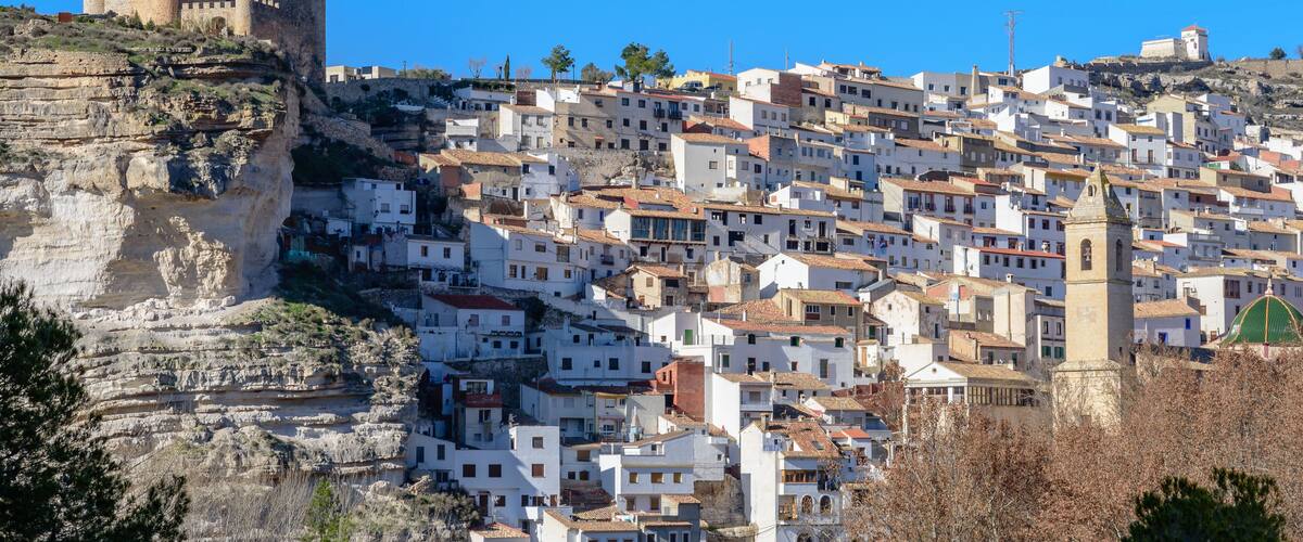 A historic town with a prominent castle on a cliff, terraced buildings, and a church with a green dome.
