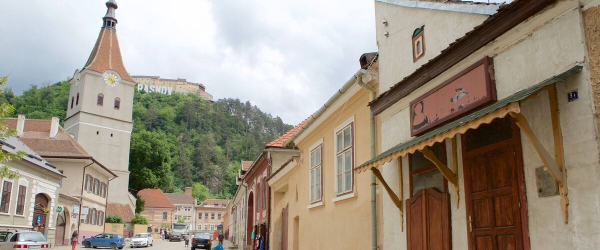 A historic town street with traditional buildings, a church tower, and a hill with a castle in the background.