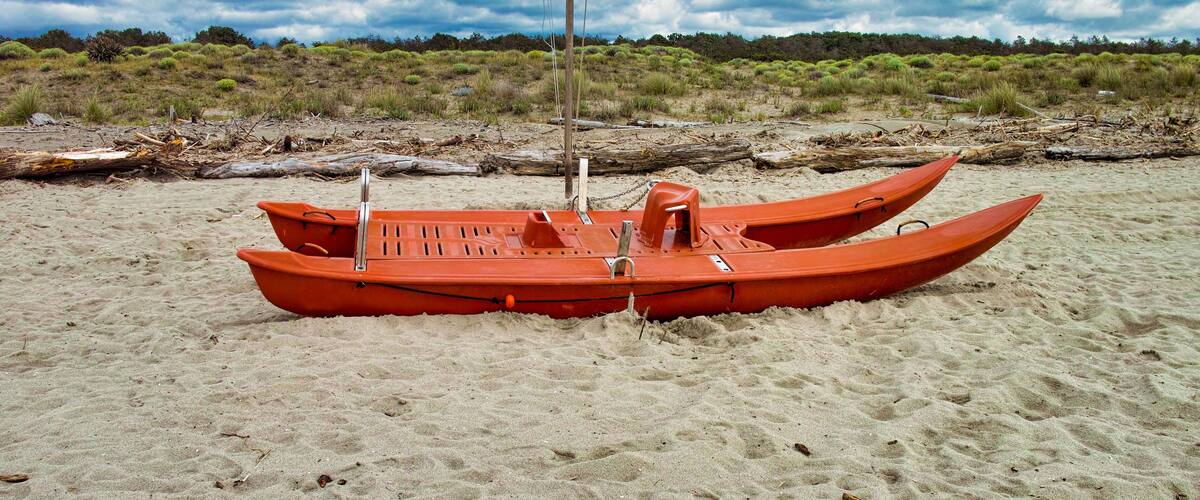 A red boat on a sandy beach with a cloudy sky and vegetation in the background.