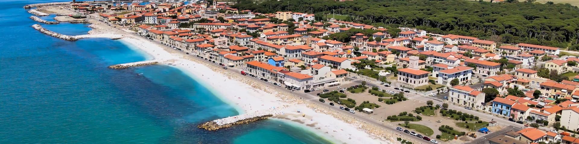A coastal town with a beach, clear blue waters, and red-roofed buildings.