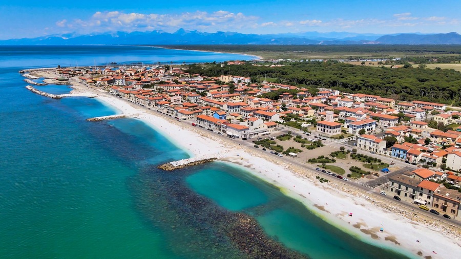Eine Küstenstadt mit Strand, klarem, blauem Wasser und Häusern mit roten Dächern.