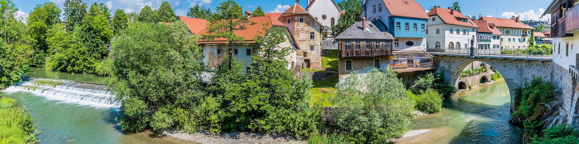 A river flowing through a town with historic buildings and a stone bridge.