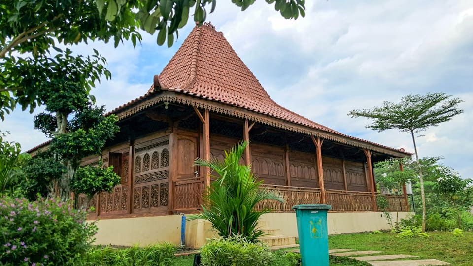 A traditional wooden building with a tiled roof, surrounded by lush greenery and a clear sky.