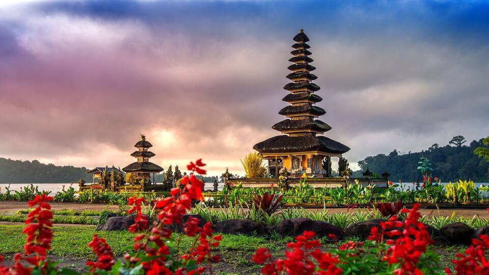 A traditional Balinese temple with tiered roofs, surrounded by lush greenery and a body of water.