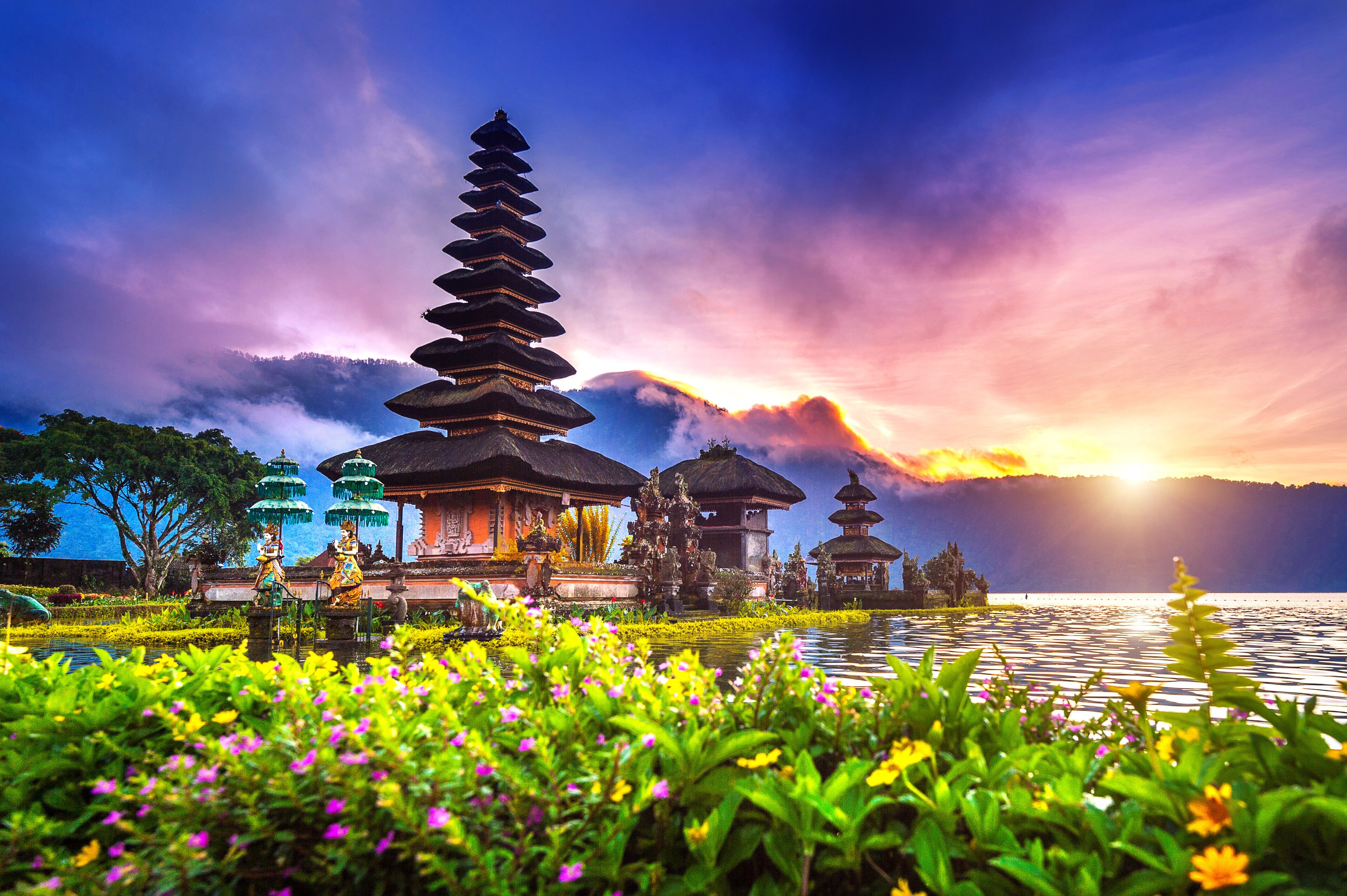 A traditional Balinese temple with tiered roofs, a lotus pond, and a sunset in the background.