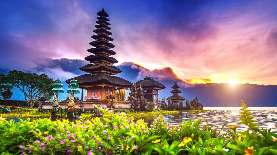 A traditional Balinese temple with tiered roofs, a lotus pond, and a sunset in the background.