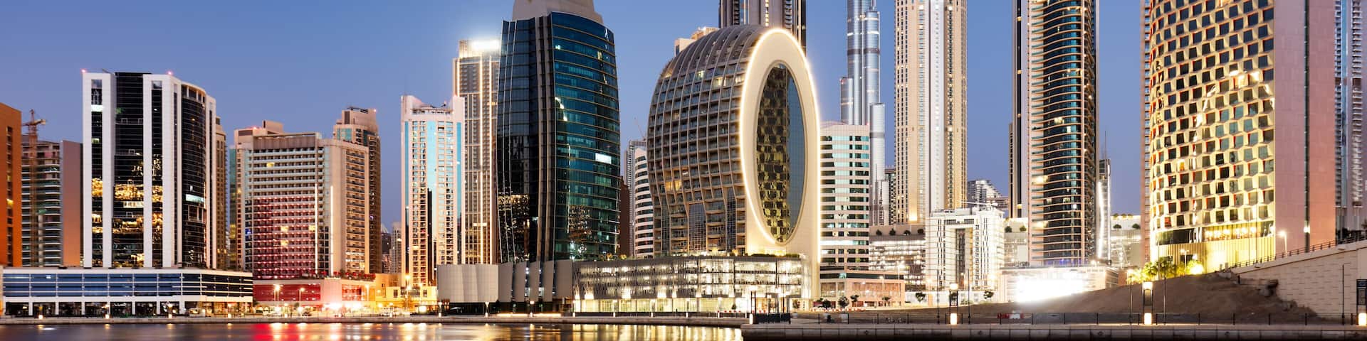 A city skyline with modern high-rise buildings, a distinctive circular structure, and a clear sky.