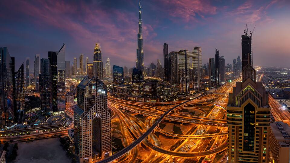 Elevated, panoramic view of the illuminated skyline of Dubai City center and busy Sheikh Zayed road intersection, United Arab Emirates, during evening time
