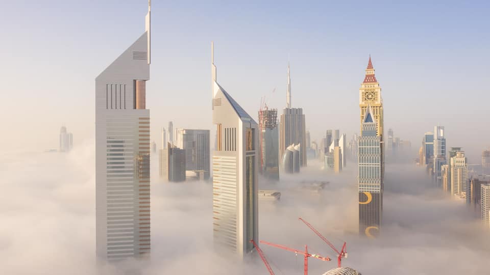 Paisagem urbana com arranha-céus modernos, incluindo uma torre distinta com topo pontiagudo e um edifício com telhado inclinado peculiar.