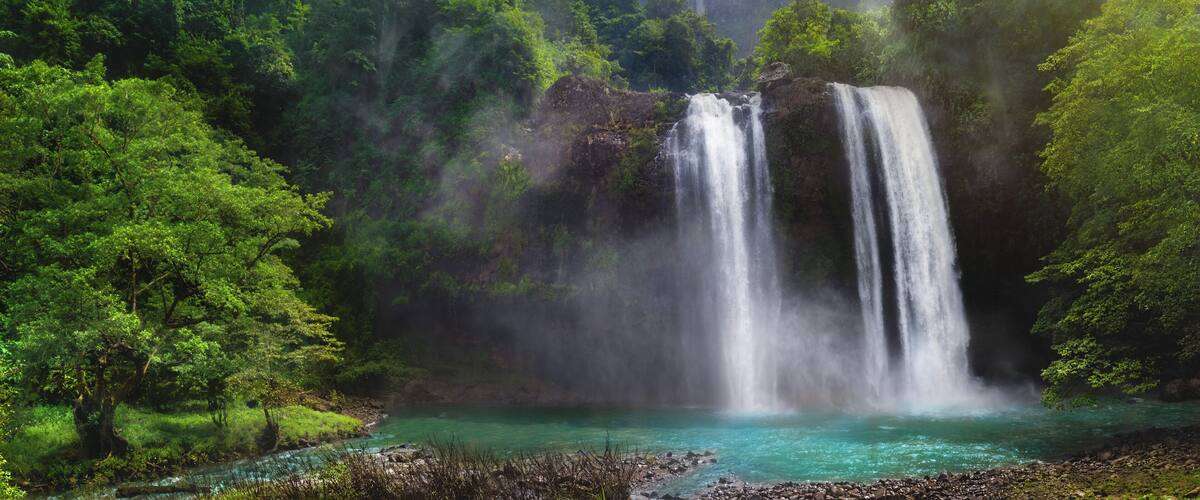 A waterfall cascading into a turquoise river surrounded by dense green forest.