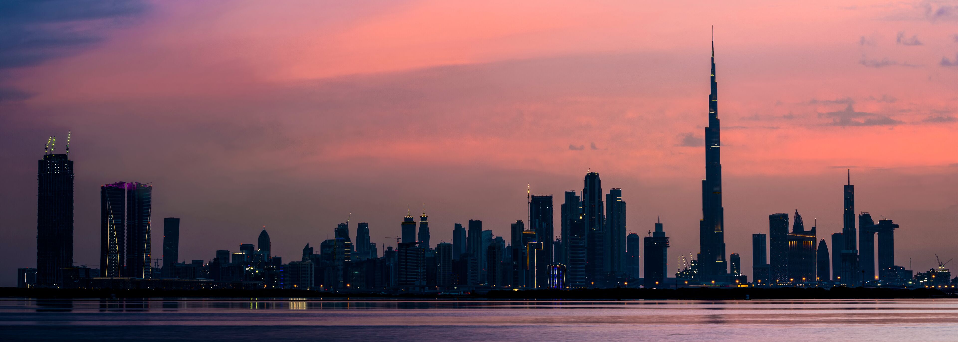 Stunning view of the illuminated Dubai skyline at dusk with the magnificent Burj Khalifa and the water canal flowing in the foreground..