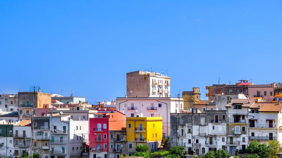 A densely packed urban area with colorful buildings, including a prominent pink and yellow structure, under a clear blue sky.