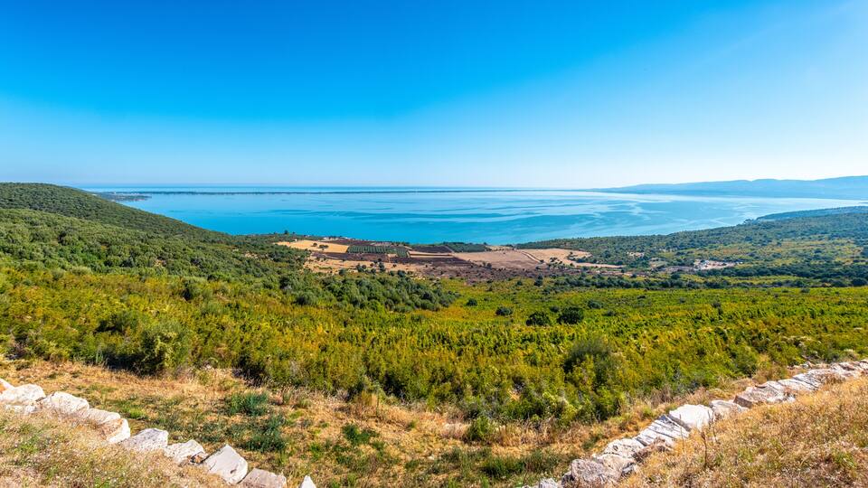 A coastal landscape with a clear view of the sea, green hills, and rocky terrain.