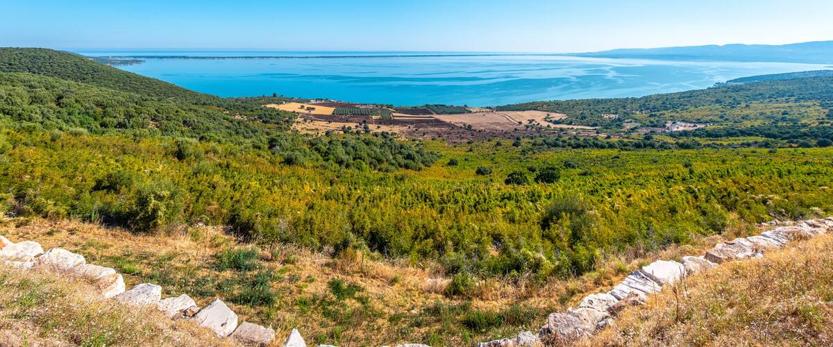 A coastal landscape with a clear view of the sea, green hills, and rocky terrain.