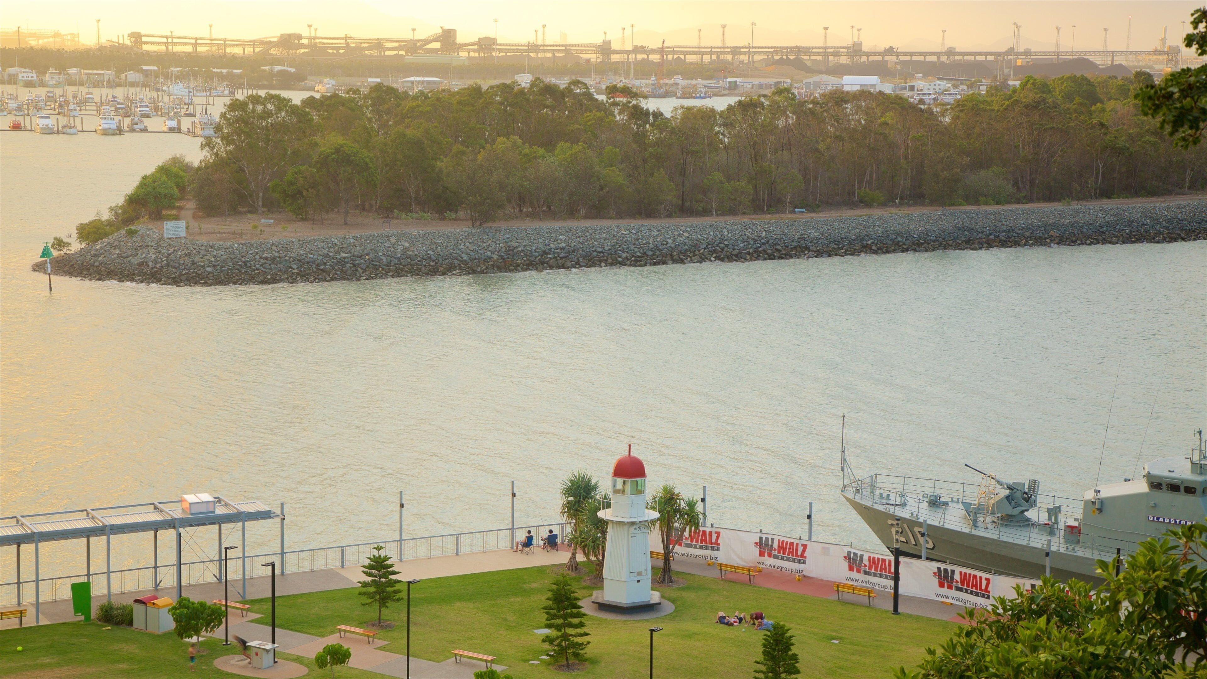 A harbor with boats, a lighthouse, a ship, and a bridge in the background.