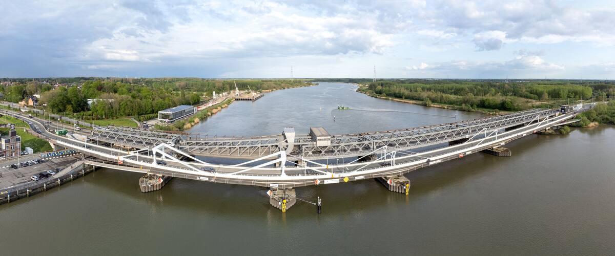 A large, white, modern bridge spanning a wide river with surrounding greenery and industrial structures.