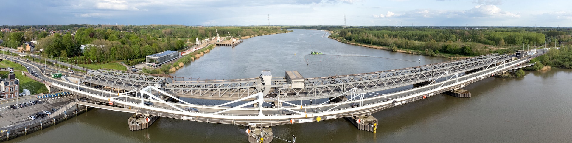 A large, white, modern bridge spanning a wide river with surrounding greenery and industrial structures.