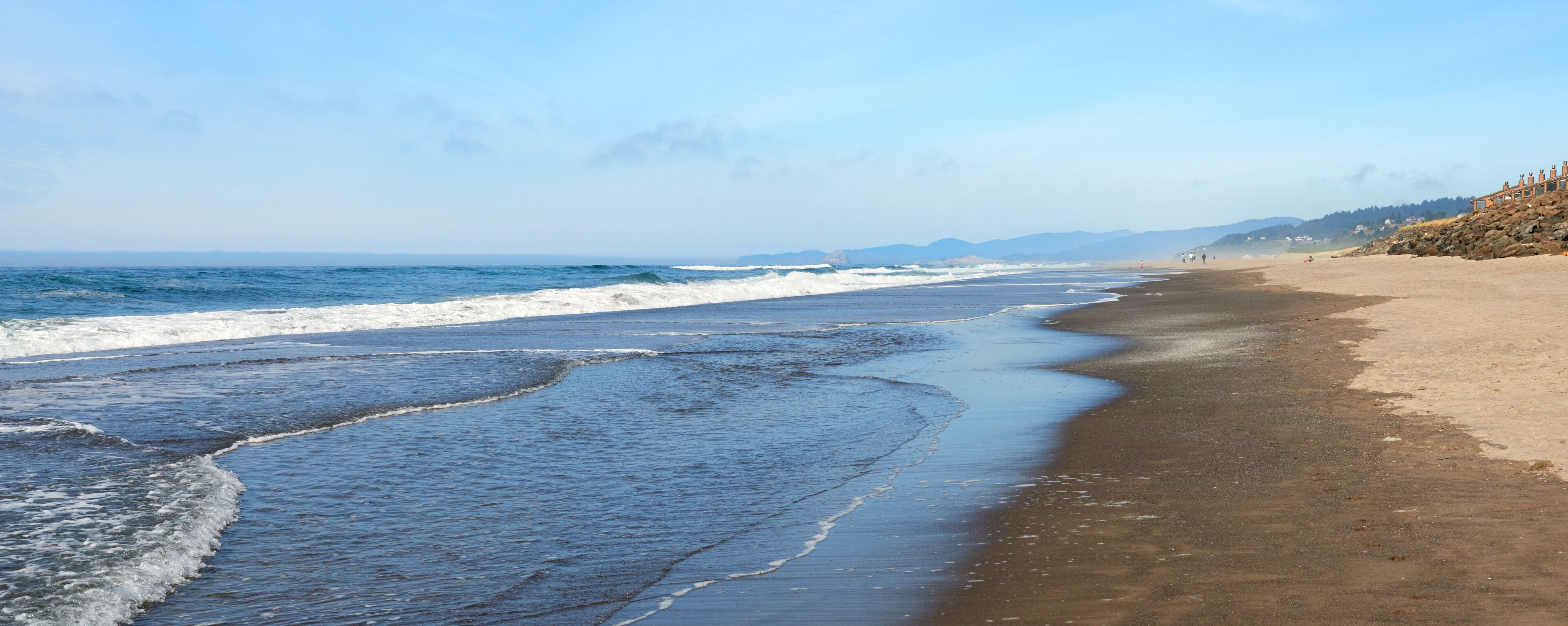 A beach with waves, a sandy shore, and distant mountains.