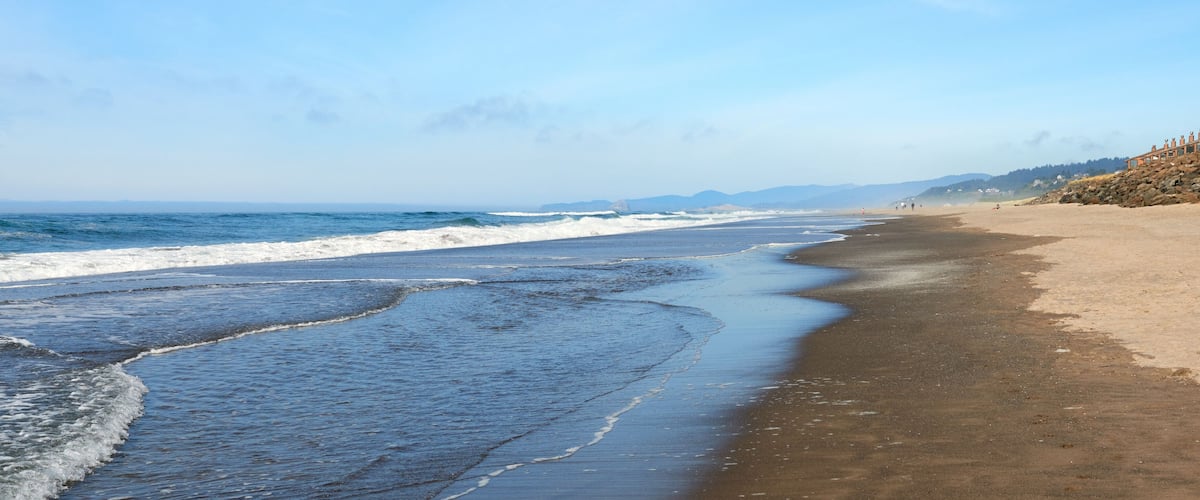 A beach with waves, a sandy shore, and distant mountains.