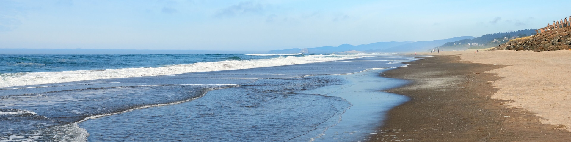 A beach with waves, a sandy shore, and distant mountains.