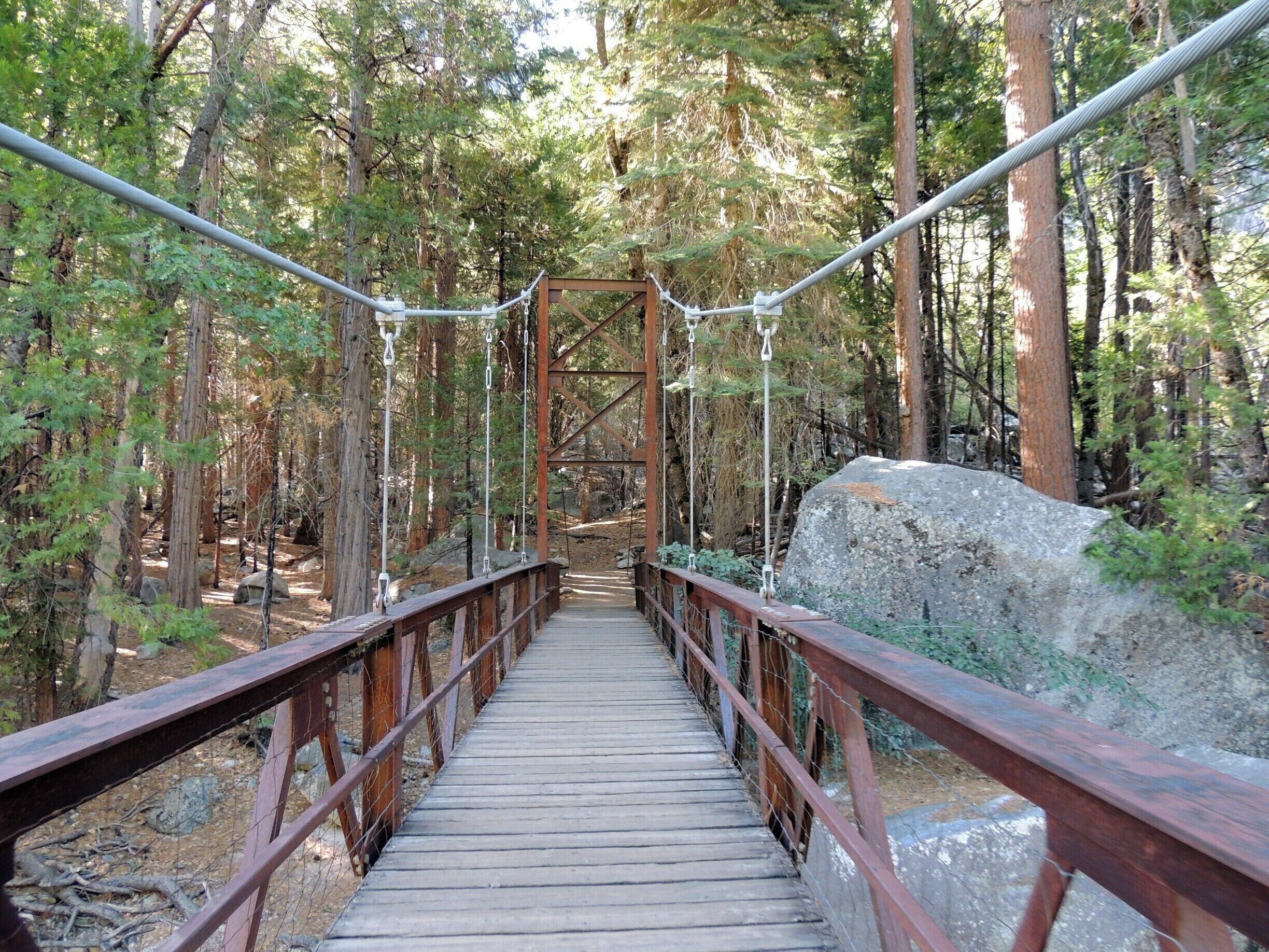 Difficult to pass up this invitation to hike Kings Canyon.  This footbridge leads to several trails in and around beautiful Zumwalt Meadows.  We took the trail to the left, a 1.5 mile, easy hike we pretty much had to ourselves.  
Be sure to bring bug spray; the gnats were so thick at times we had to keep moving or risk getting carried away during our early morning hike.   
Check out the full story at http://www.aplacecalledroam.com/home/a-walk-in-the-woods-in-kings-canyon-proves-ghostly.  