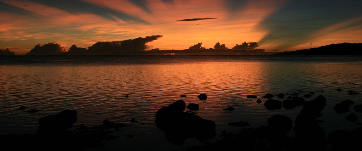 A sunset over a calm lake with rocks in the foreground.
