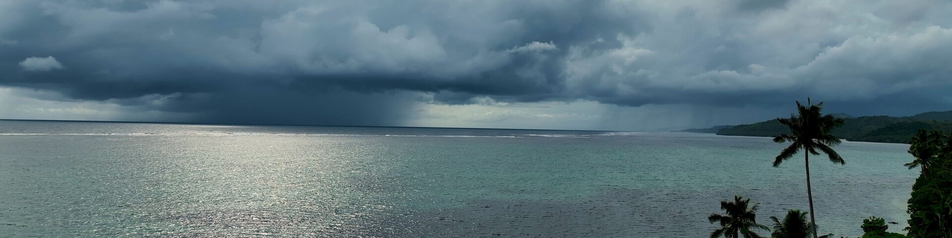 Praia com água cristalina, palmeiras e céu nublado.