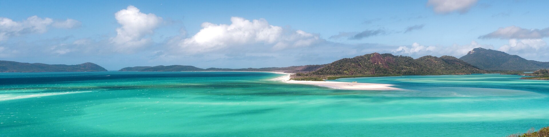 Un mar turquesa con una playa de arena blanca y colinas verdes exuberantes al fondo.