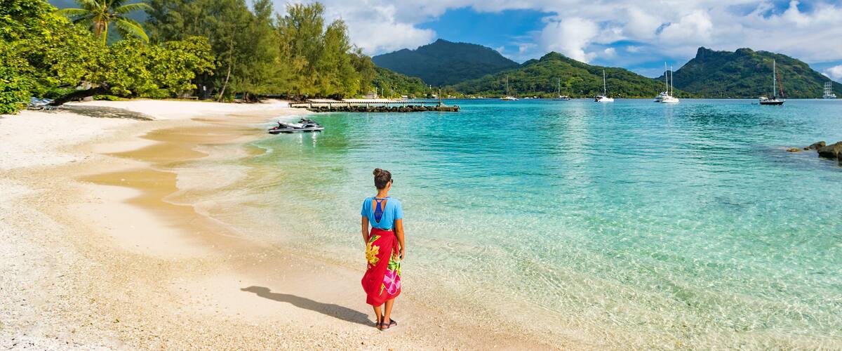 Travel tourist woman at French Polynesia beach on Huahine island cruise excursion on Tahiti holiday vacaton. Girl wearing polynesian sarong skirt banner panorama crop.