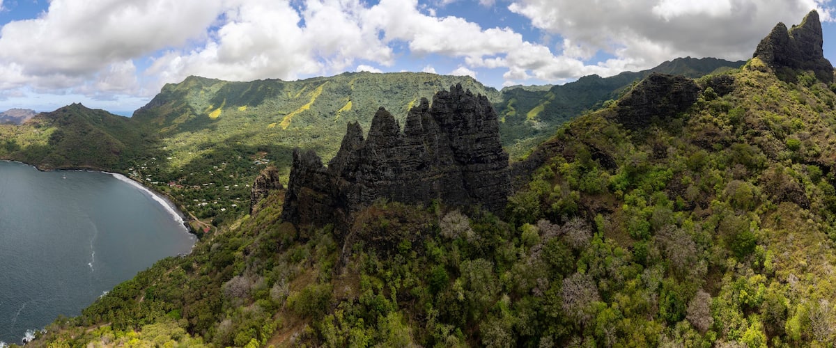 A coastal landscape with a rugged coastline, dense green forest, and a prominent rocky peak.