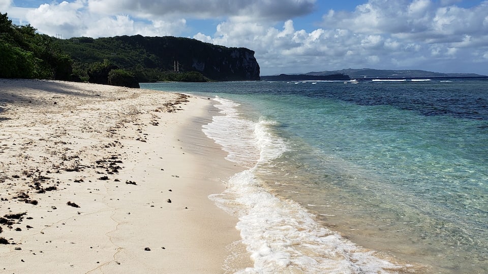 A beach with clear turquoise water, white sand, and a rocky cliff in the background.