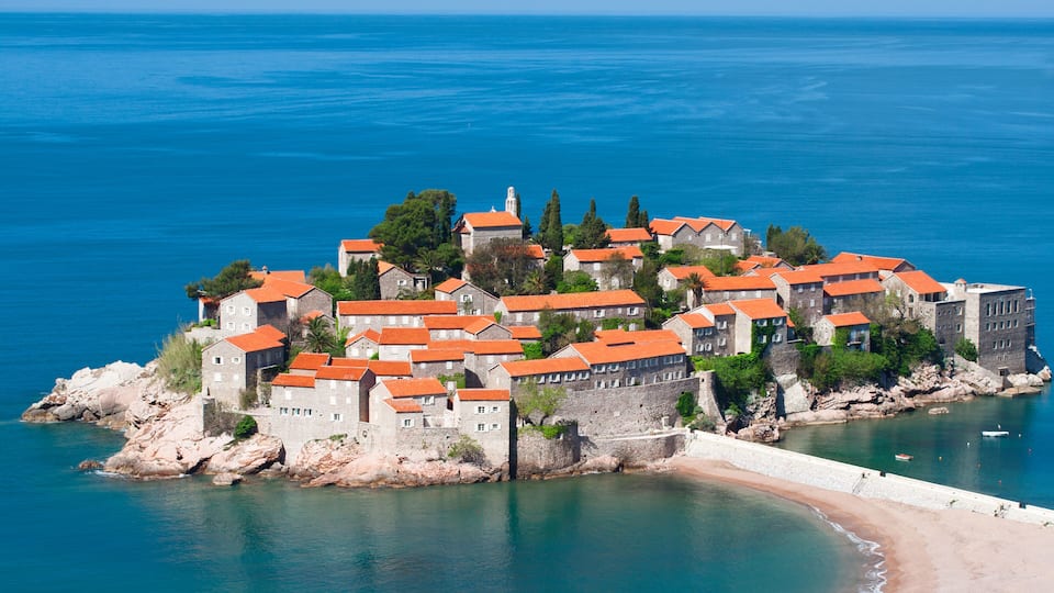 A coastal town with stone buildings and red roofs, surrounded by the sea and rocky terrain.