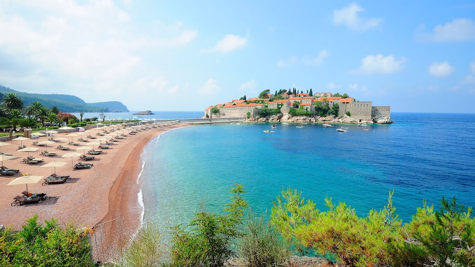 A coastal town with a beach, boats, and a castle-like structure.