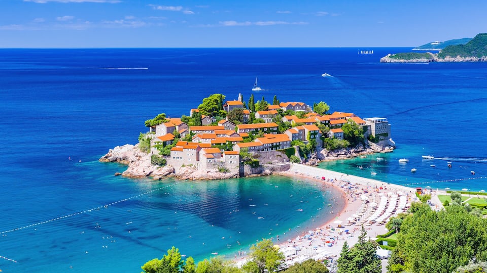 A coastal town with a beach, a lighthouse, and a cluster of buildings with red roofs.