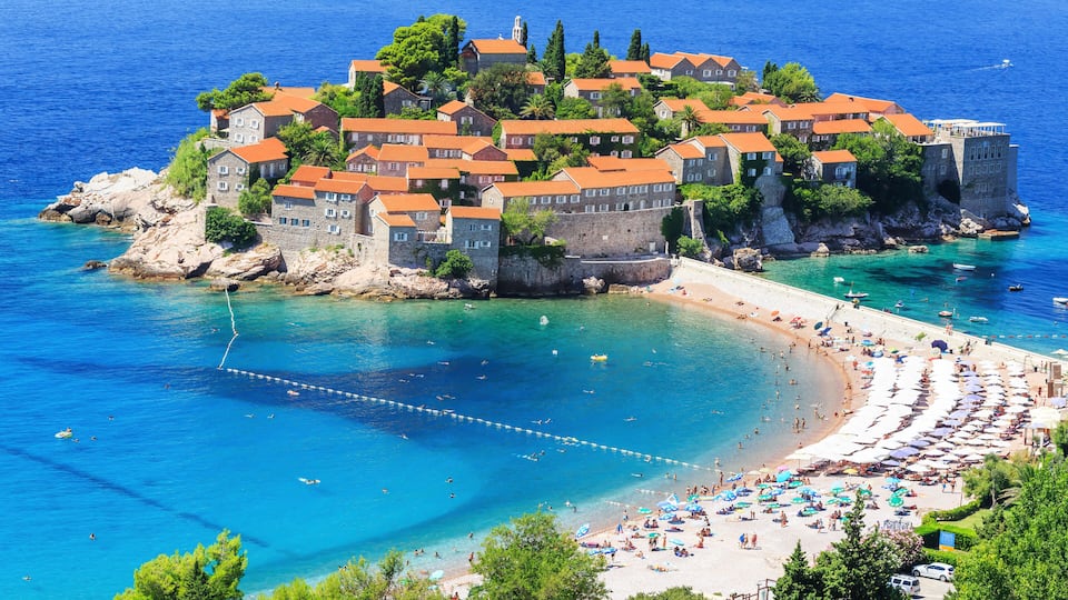 A coastal town with historic buildings, a beach, and clear blue waters.
