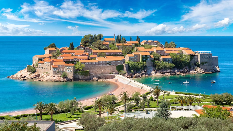 A coastal town with historic buildings, a beach, and a clear blue sea.