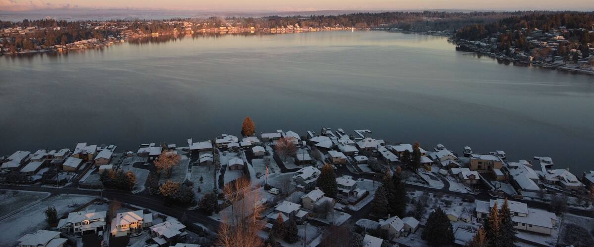 Zona residencial coberta de neu, amb cases i una gran massa d'aigua al fons.