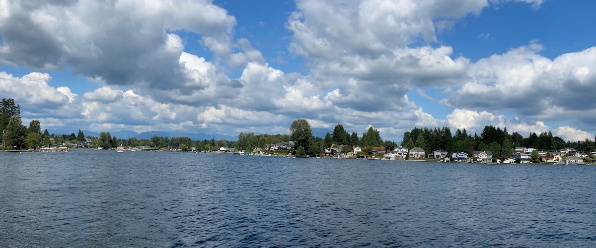 A lake with a town on the shore, surrounded by trees and mountains in the background.