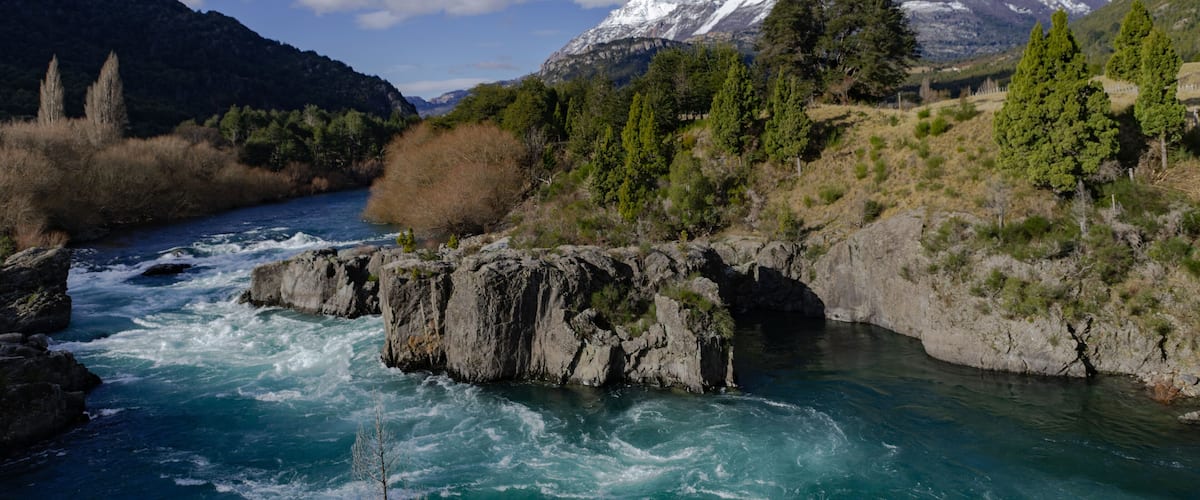 A river flowing through a mountainous landscape with snow-capped peaks in the background.