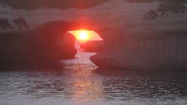 A sunset through a natural rock arch over water.