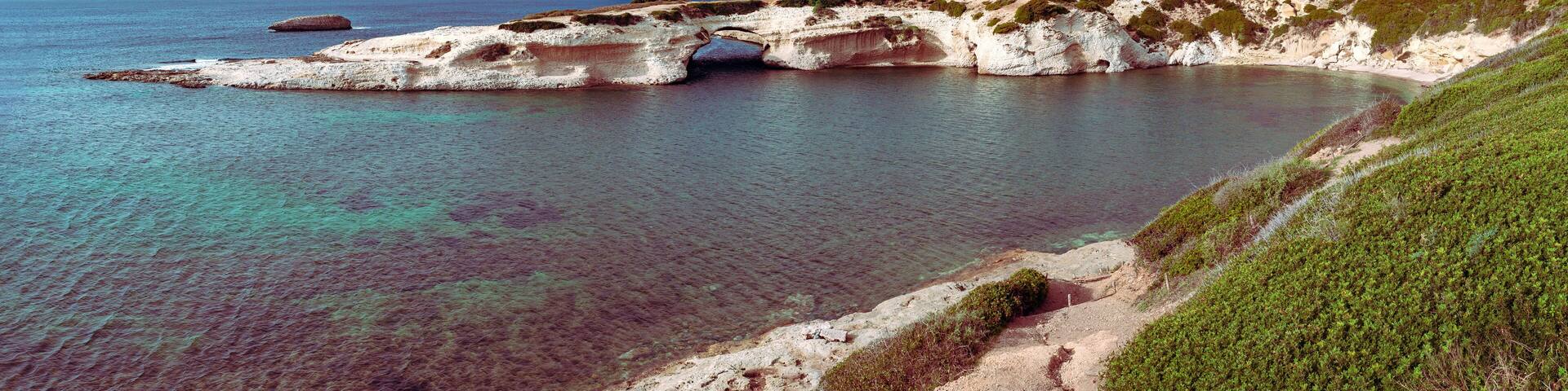 A coastal landscape with cliffs, a clear blue sea, and a small bridge.