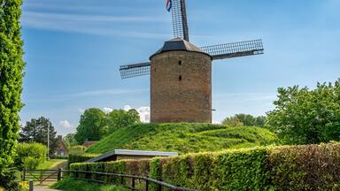 A traditional windmill on a grassy hill with a clear blue sky.