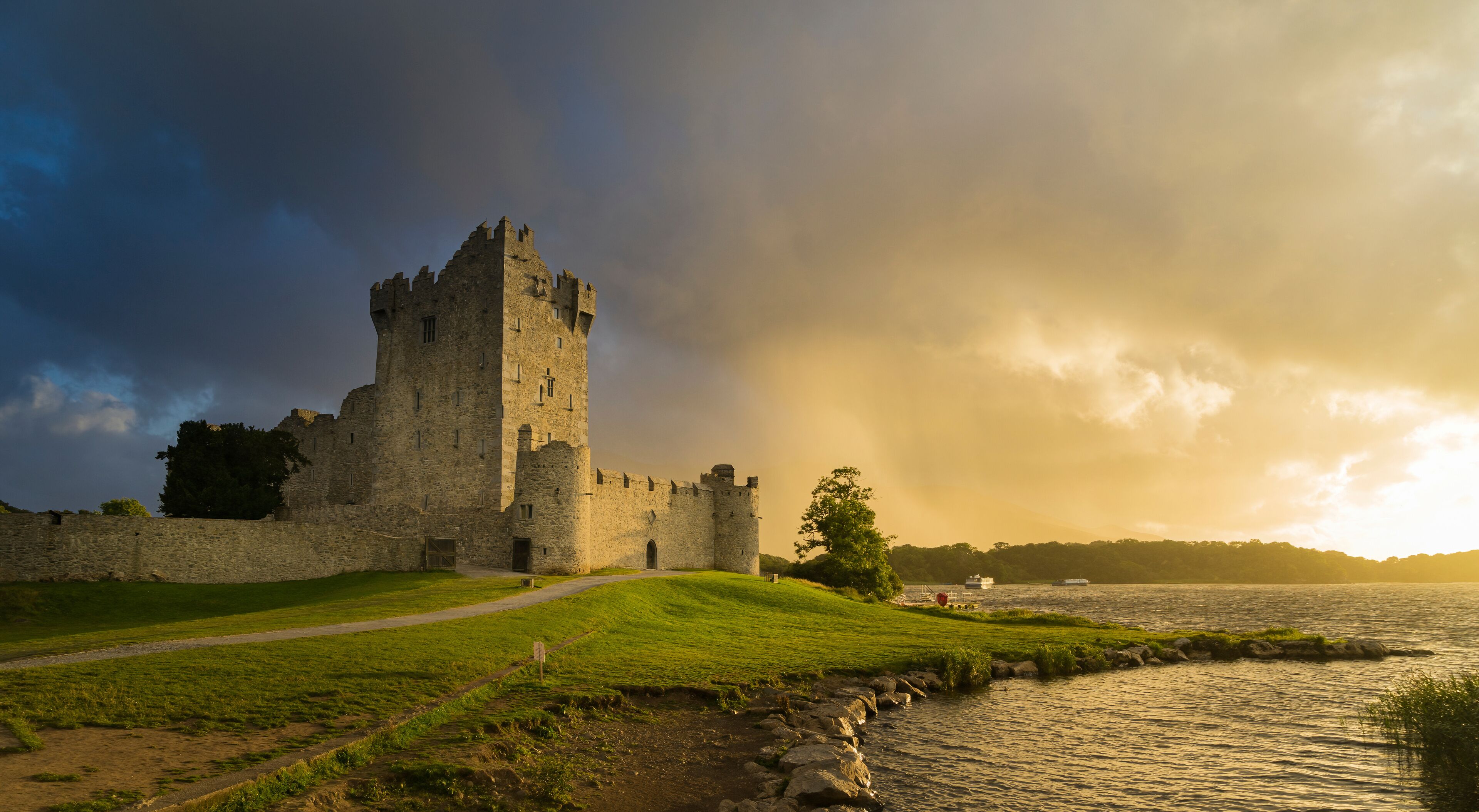 View of the ruins of Ros Castle at sunset under cloudy skies. Medieval castle on the shores of Loch Leane in Killarney National Park, County Kerry.