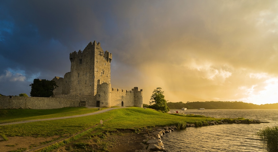 View of the ruins of Ros Castle at sunset under cloudy skies. Medieval castle on the shores of Loch Leane in Killarney National Park, County Kerry.