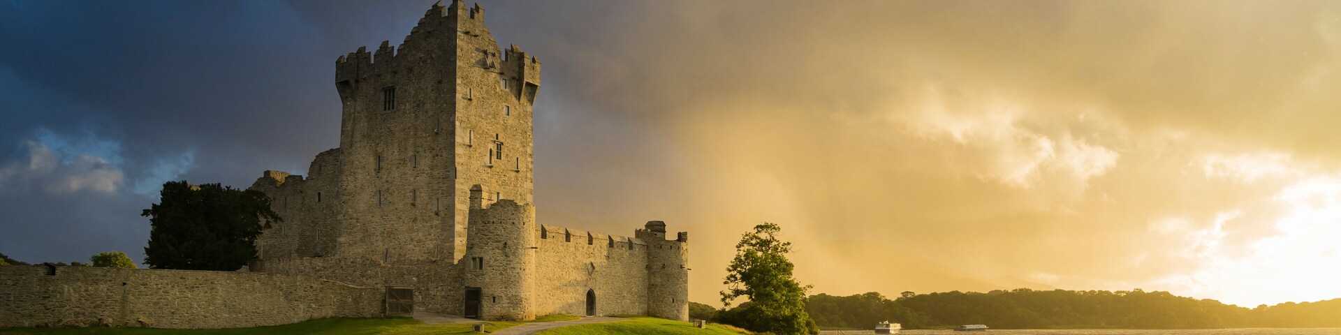 A historic castle with a tall tower, surrounded by a grassy area and a body of water.