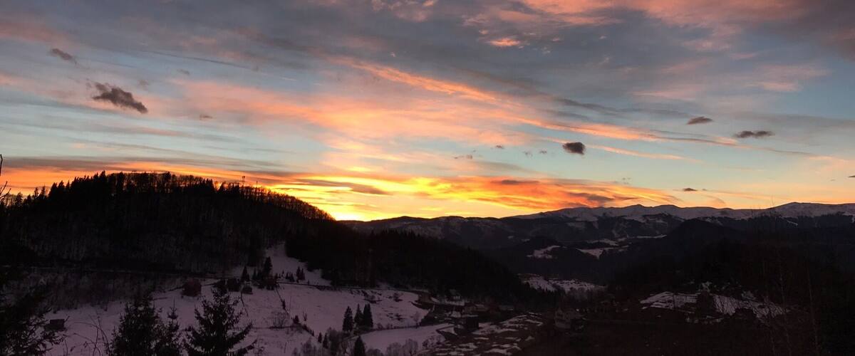 A mountainous landscape with a sunset and a forested area.